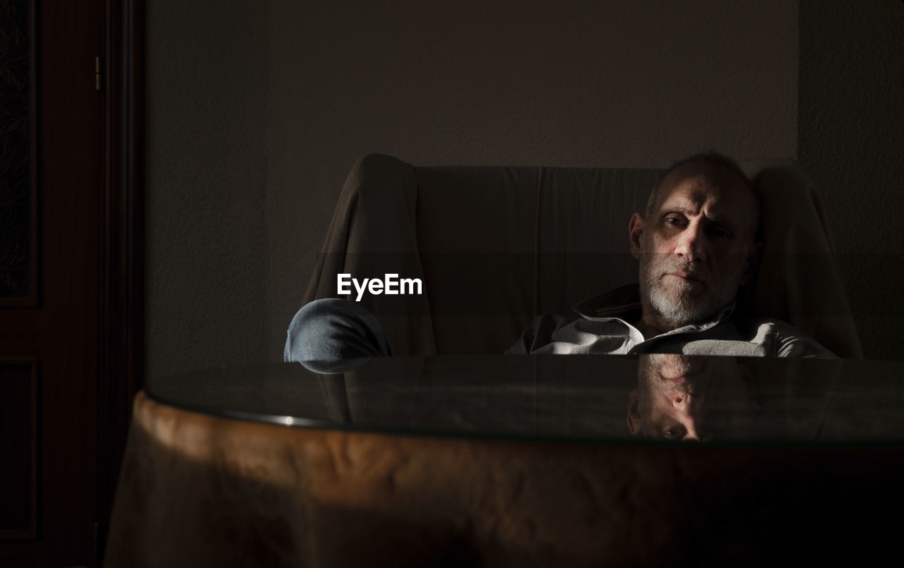 Adult man sitting on sofa chair in living room with sunlight and shadow