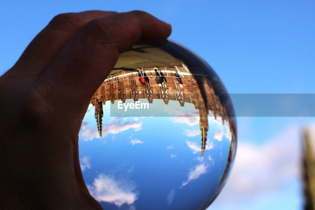 Close-up of human hand holding crystal ball against blue sky