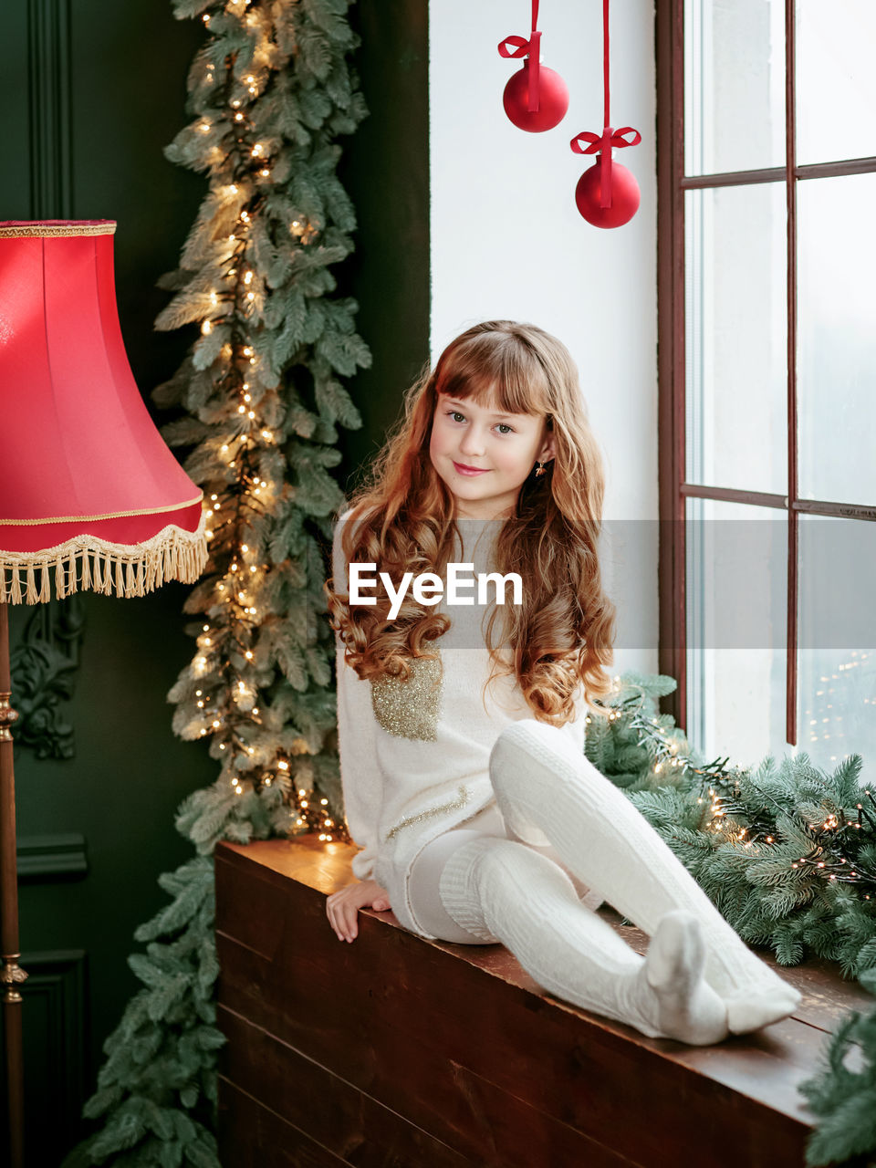 Happy young girl sitting by the window and christmas tree