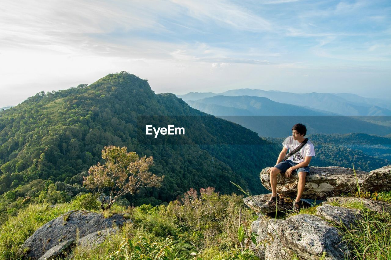 Man looking at mountain while sitting on cliff against sky