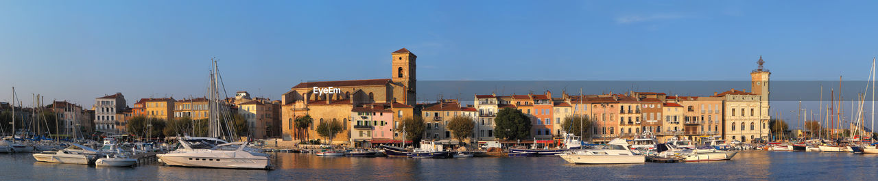 SAILBOATS MOORED IN HARBOR AGAINST BUILDINGS IN CITY