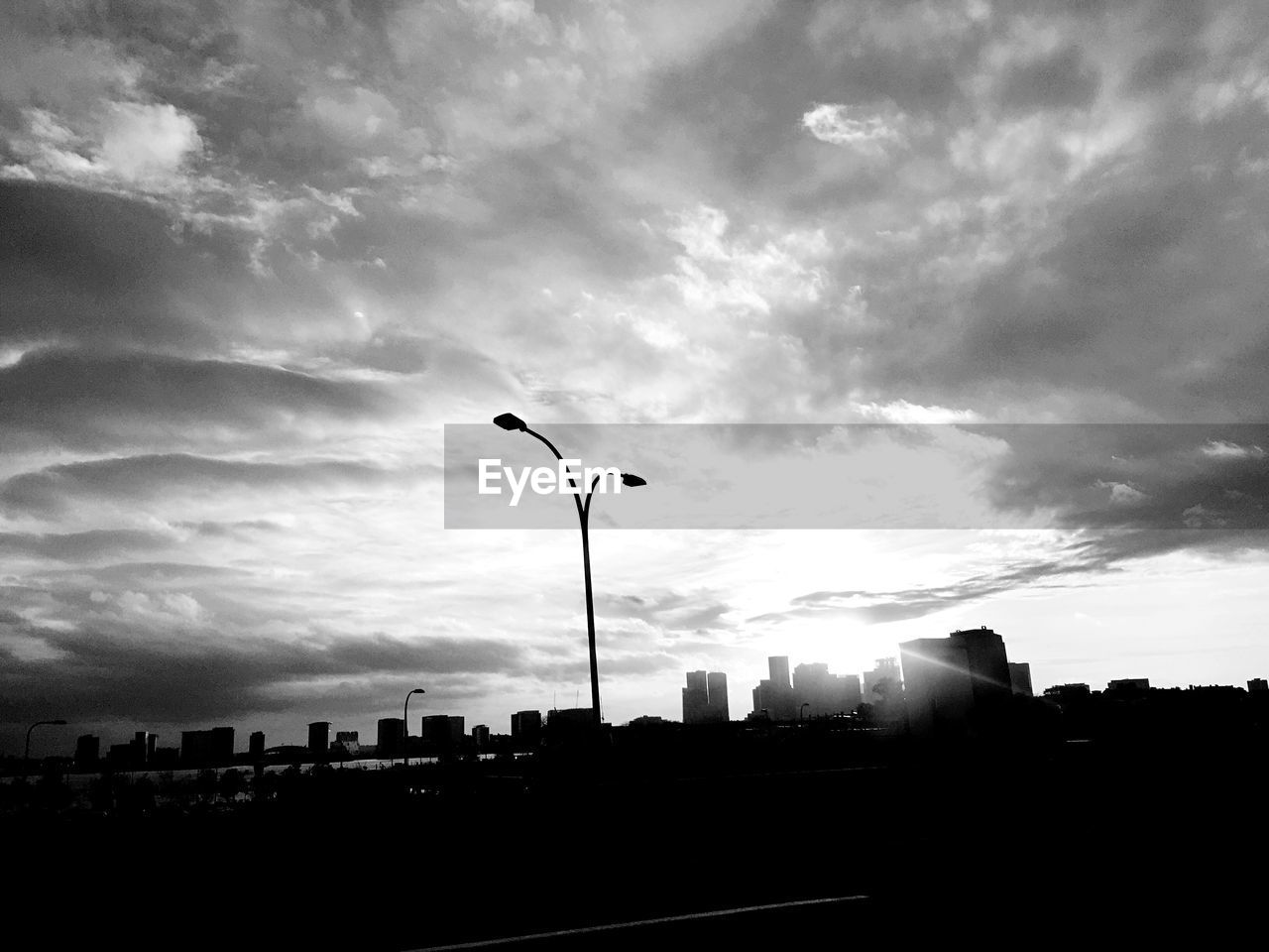 Low angle view of silhouette street light and buildings against cloudy sky