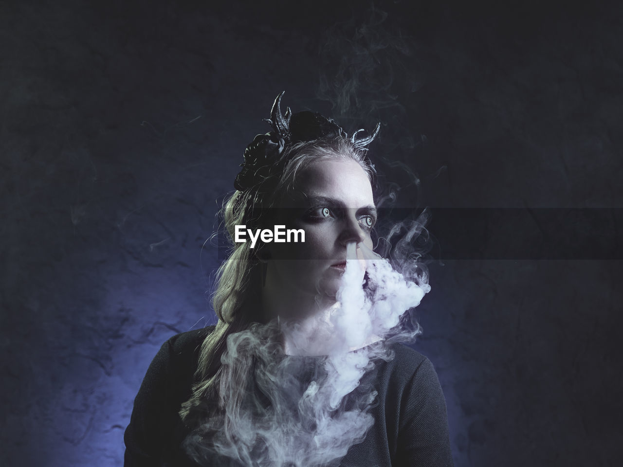 Spooky young woman emitting smoke from nose against black background