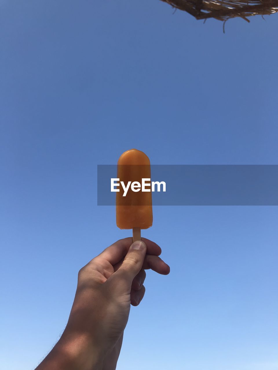 Cropped hand of person holding popsicle against clear sky