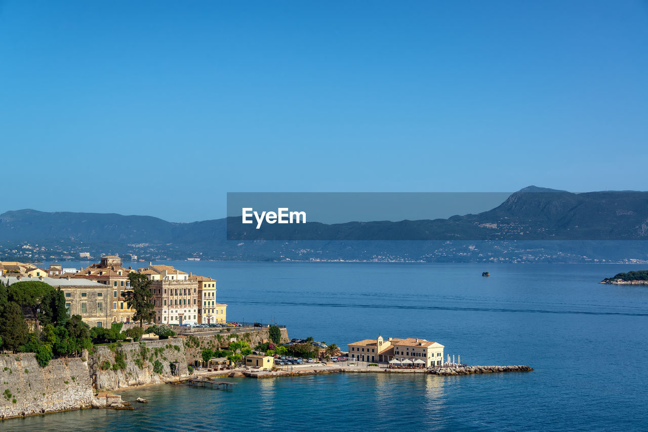 Sea by buildings against clear blue sky