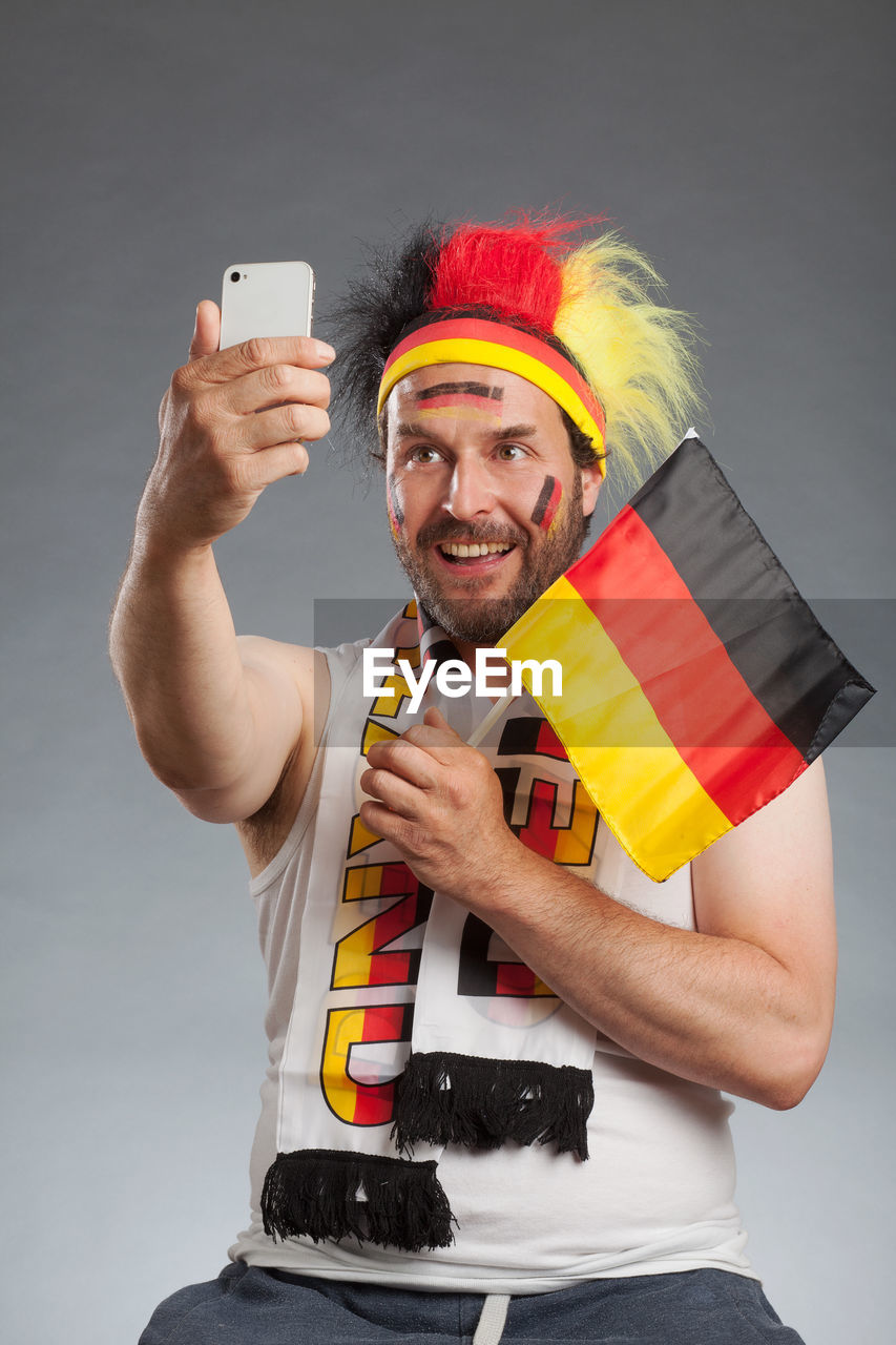 Happy soccer fan holding german flag while taking selfie against gray background