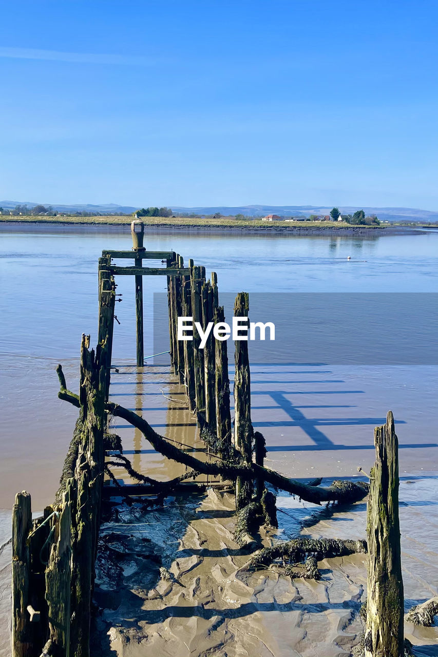 Wooden posts in sea against sky