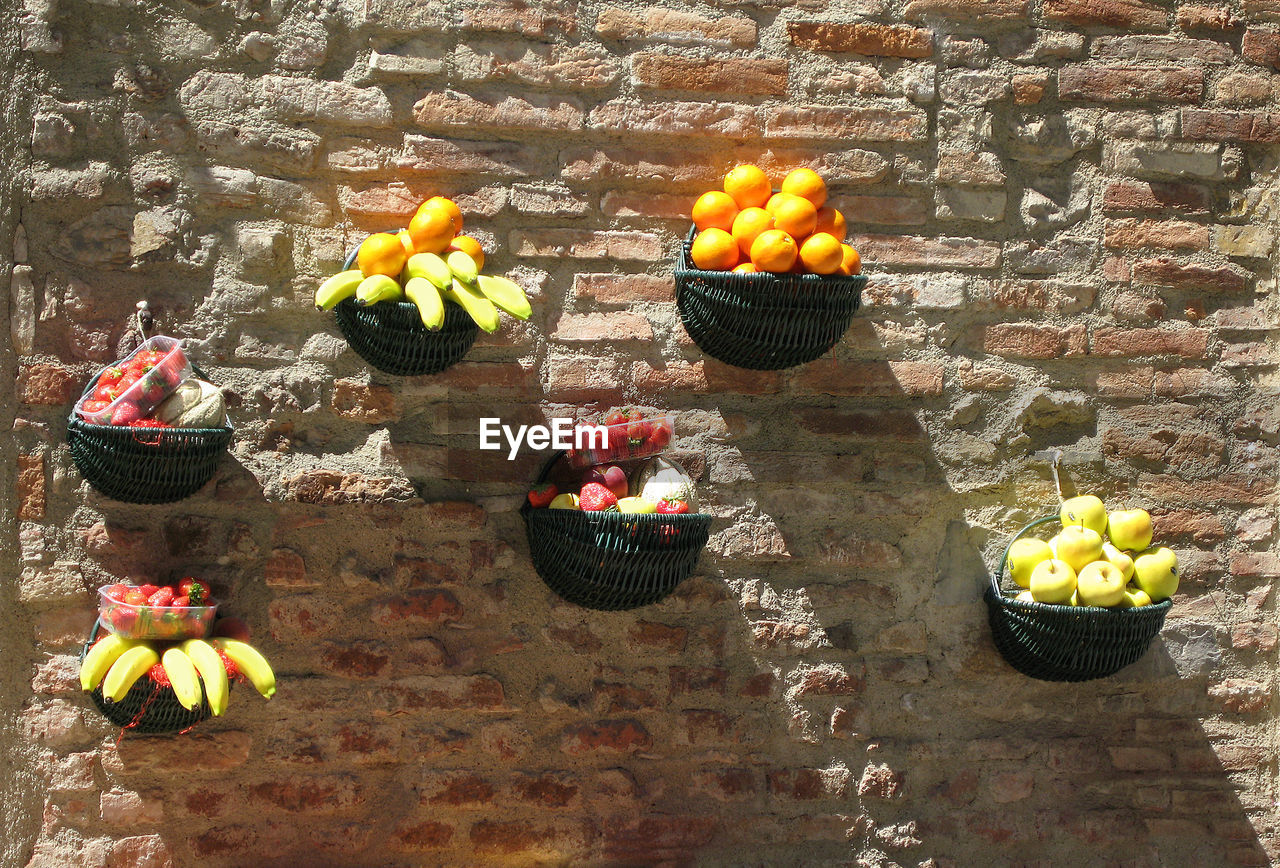 Fruits in baskets hanging from brick wall