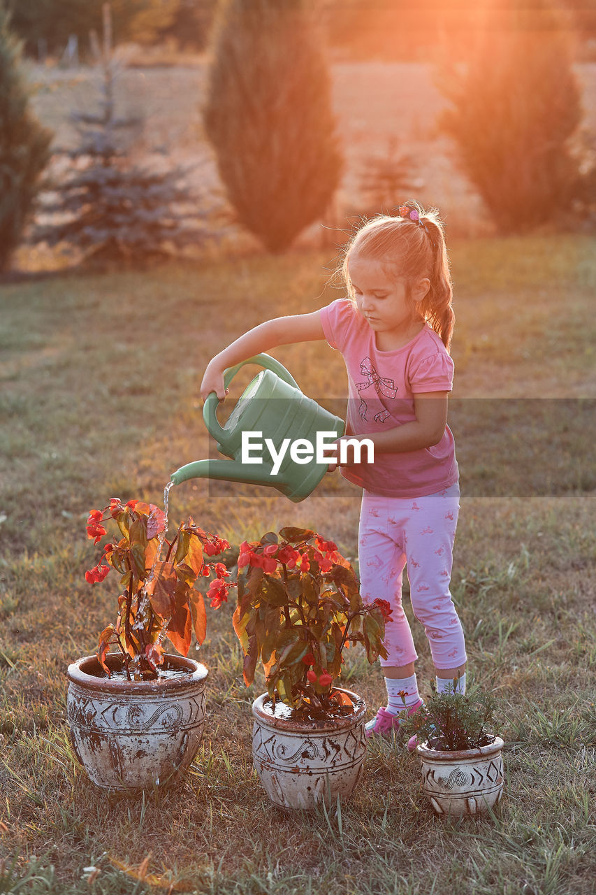 Girl watering plants while standing on grass