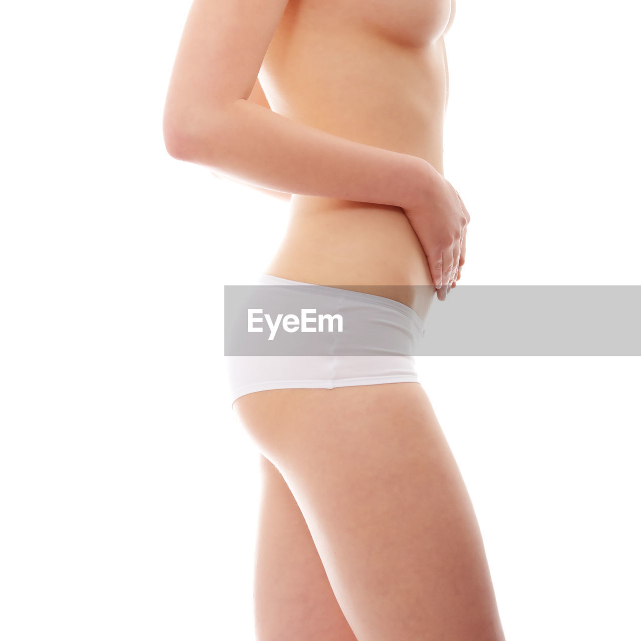 Midsection of shirtless woman touching belly against white background
