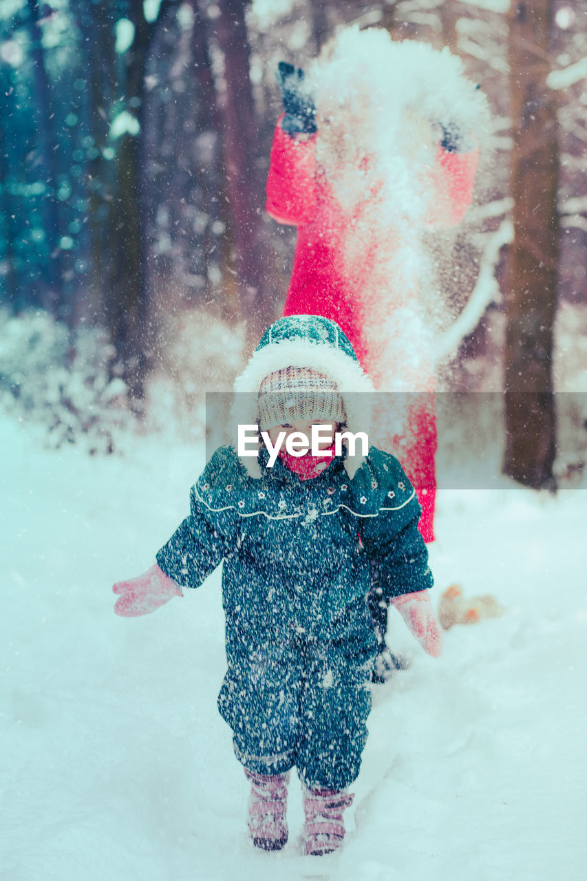 Mother and daughter wearing warm clothing playing in snow during winter