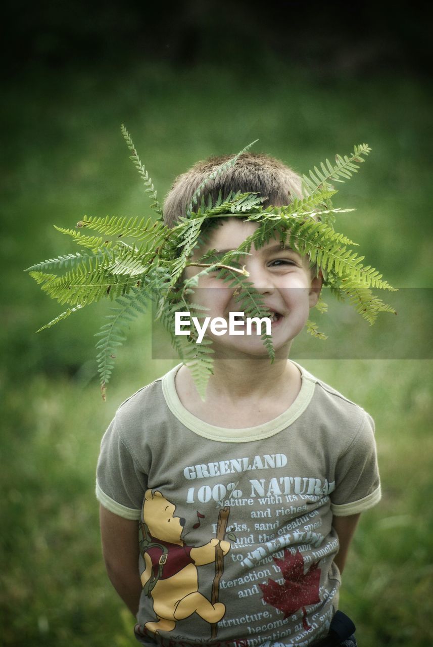 Portrait of cute boy with ferns on head at field