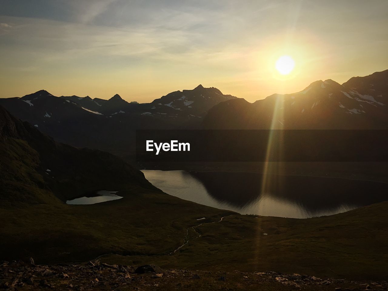 Idyllic shot of sunlight on lake in mountain range against sky during sunrise