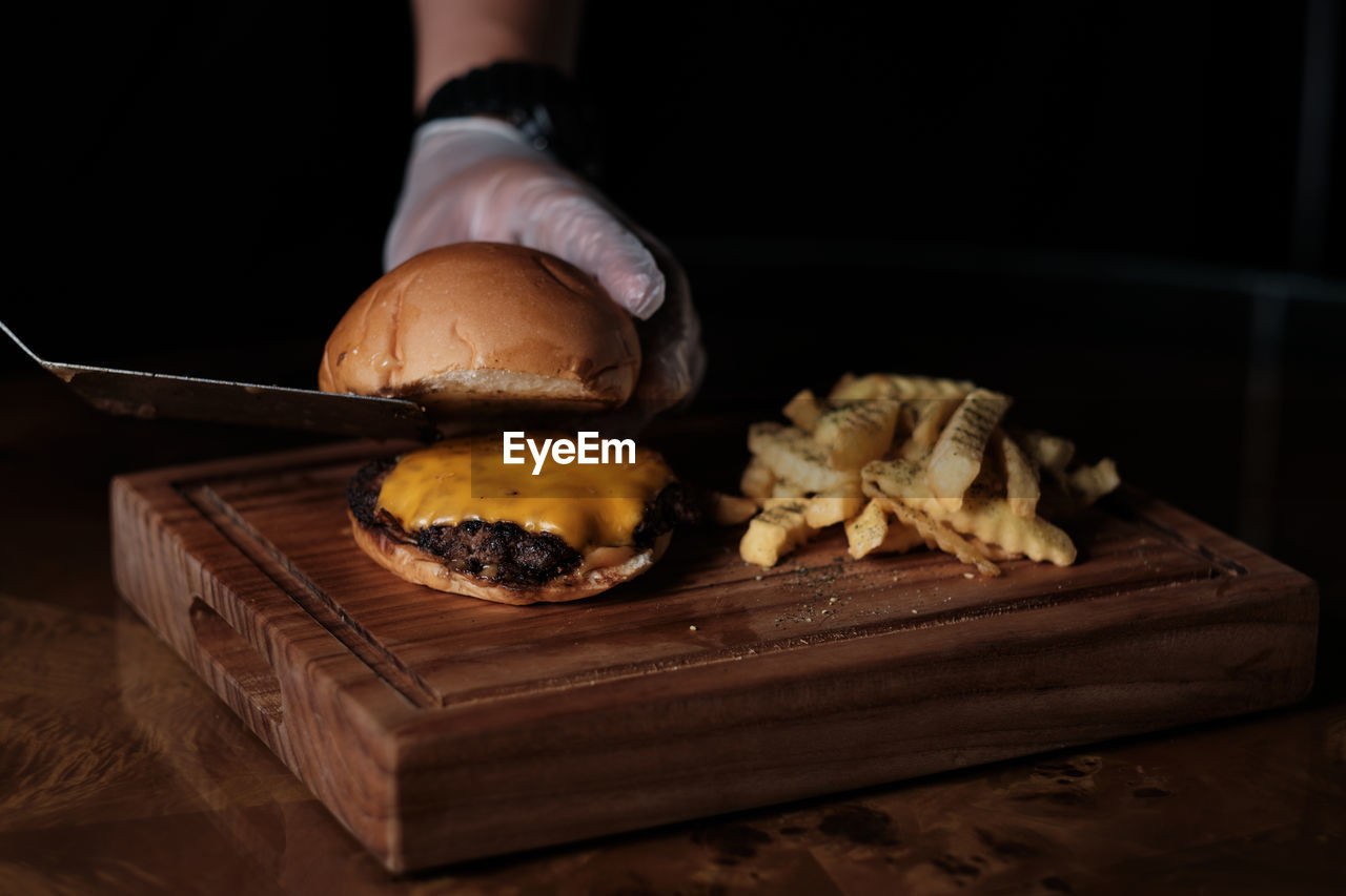 Cropped hand of chef cutting hamburger