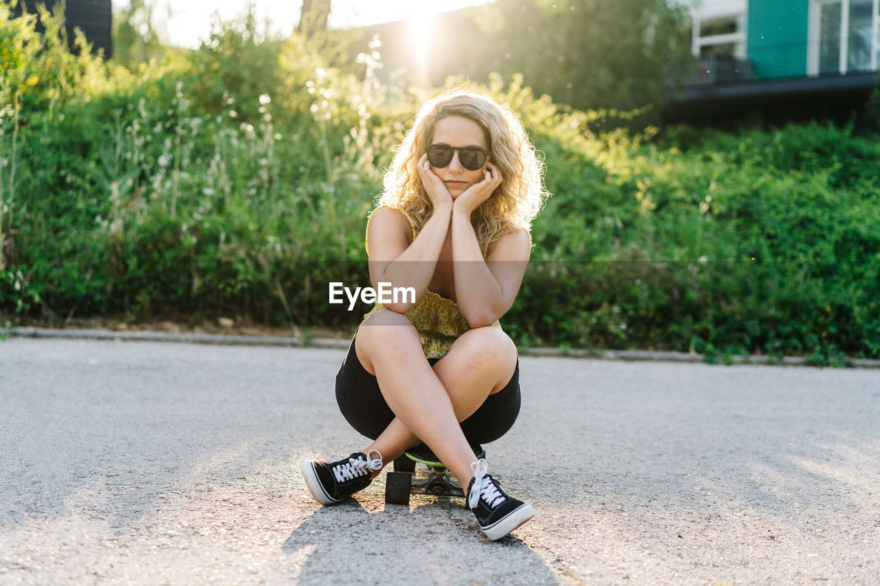 Young woman wearing sunglasses sitting on road