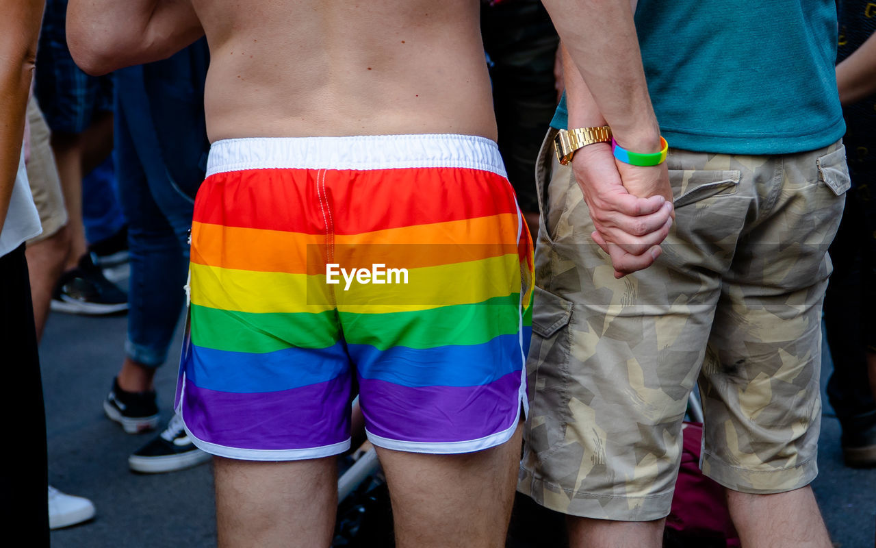 Midsection of gay couple holding hands while standing in parade