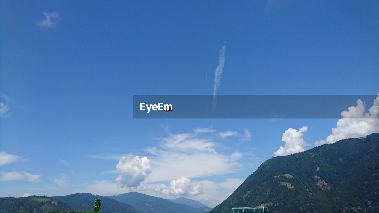 LOW ANGLE VIEW OF AIRPLANE FLYING OVER MOUNTAINS AGAINST BLUE SKY