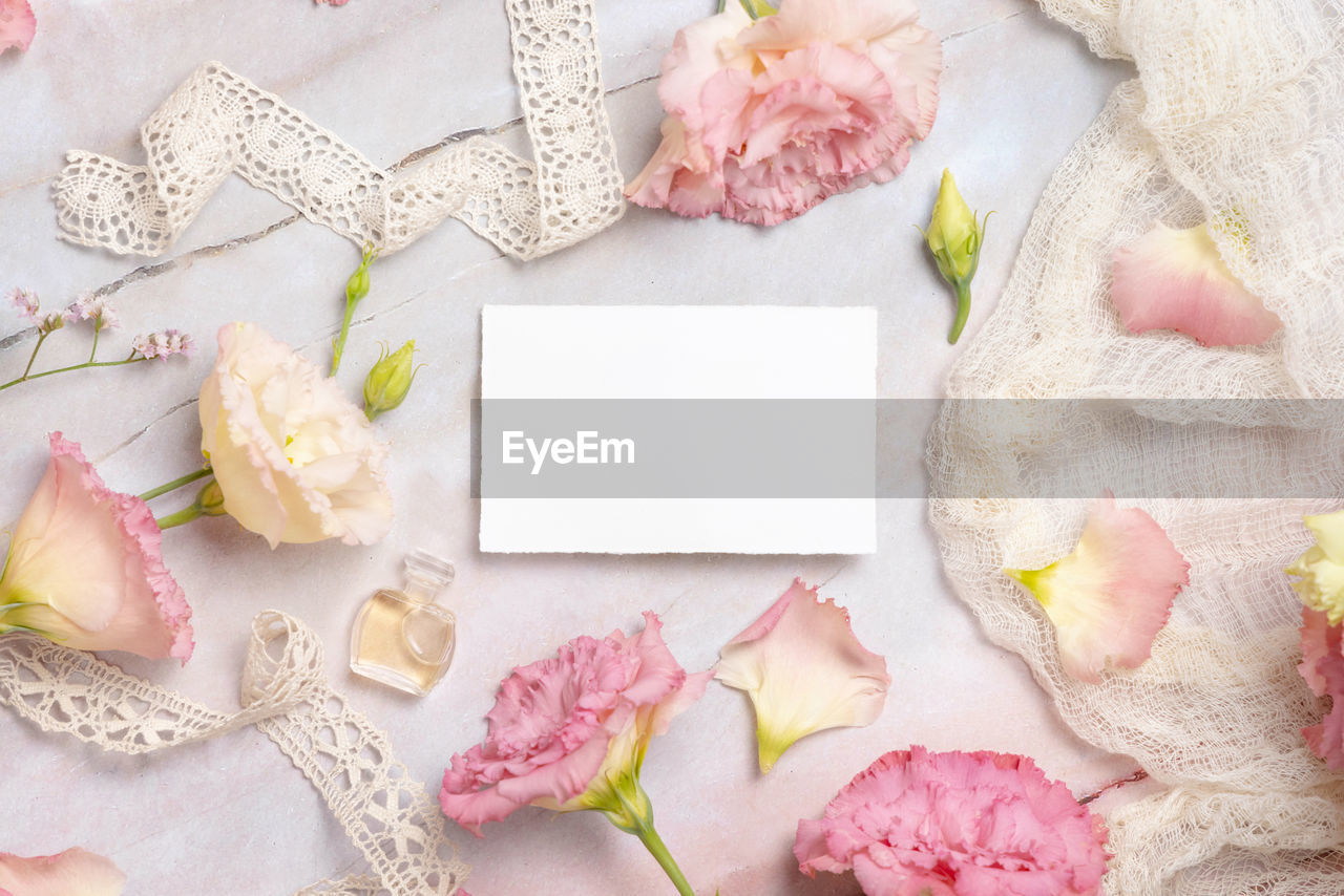 Pink flowers and a blank greeting card laying on a marble table 