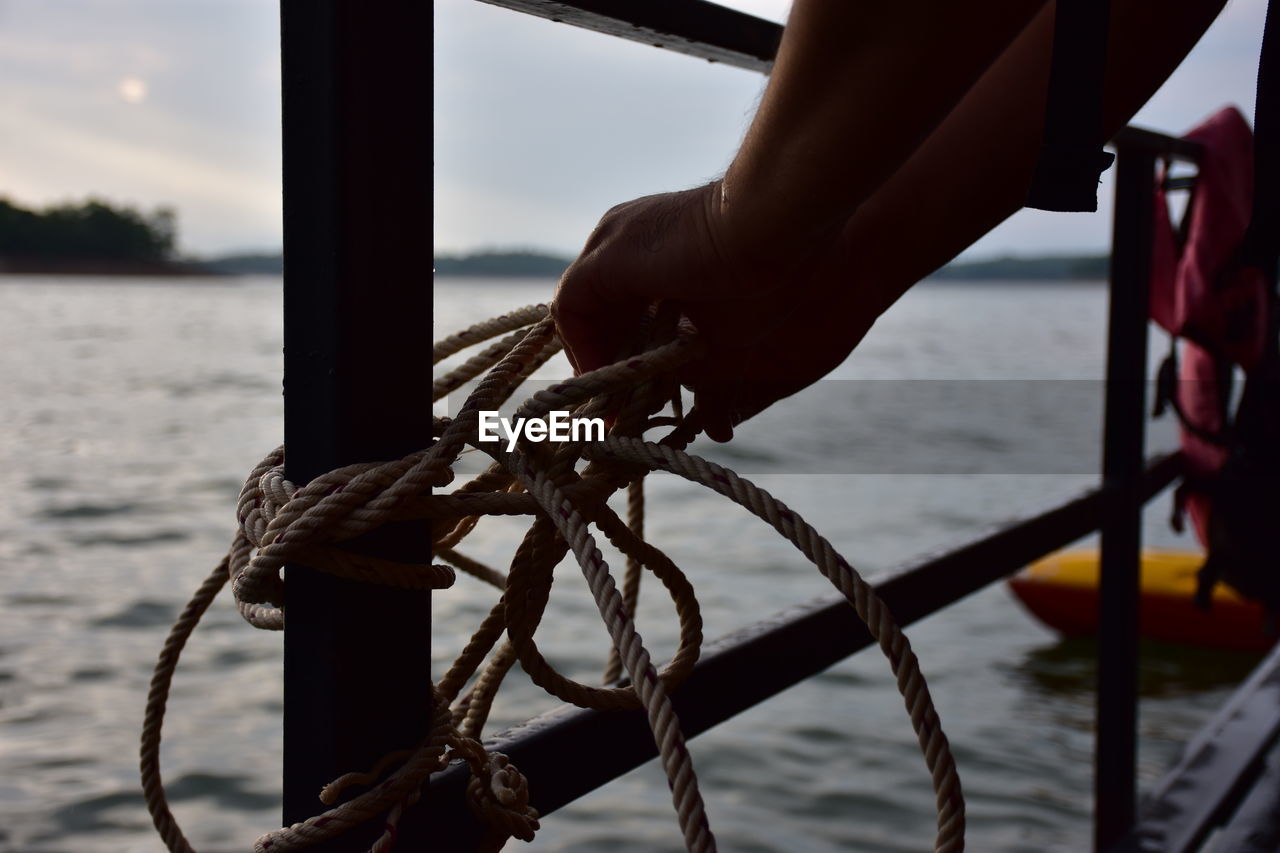 Close-up of hands tying rope to railing