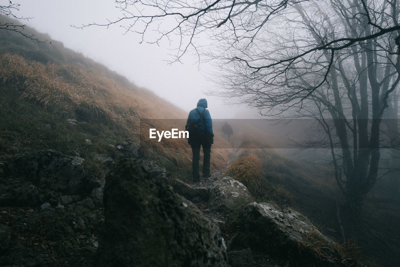 Rear view of person hiking on mountain in foggy weather