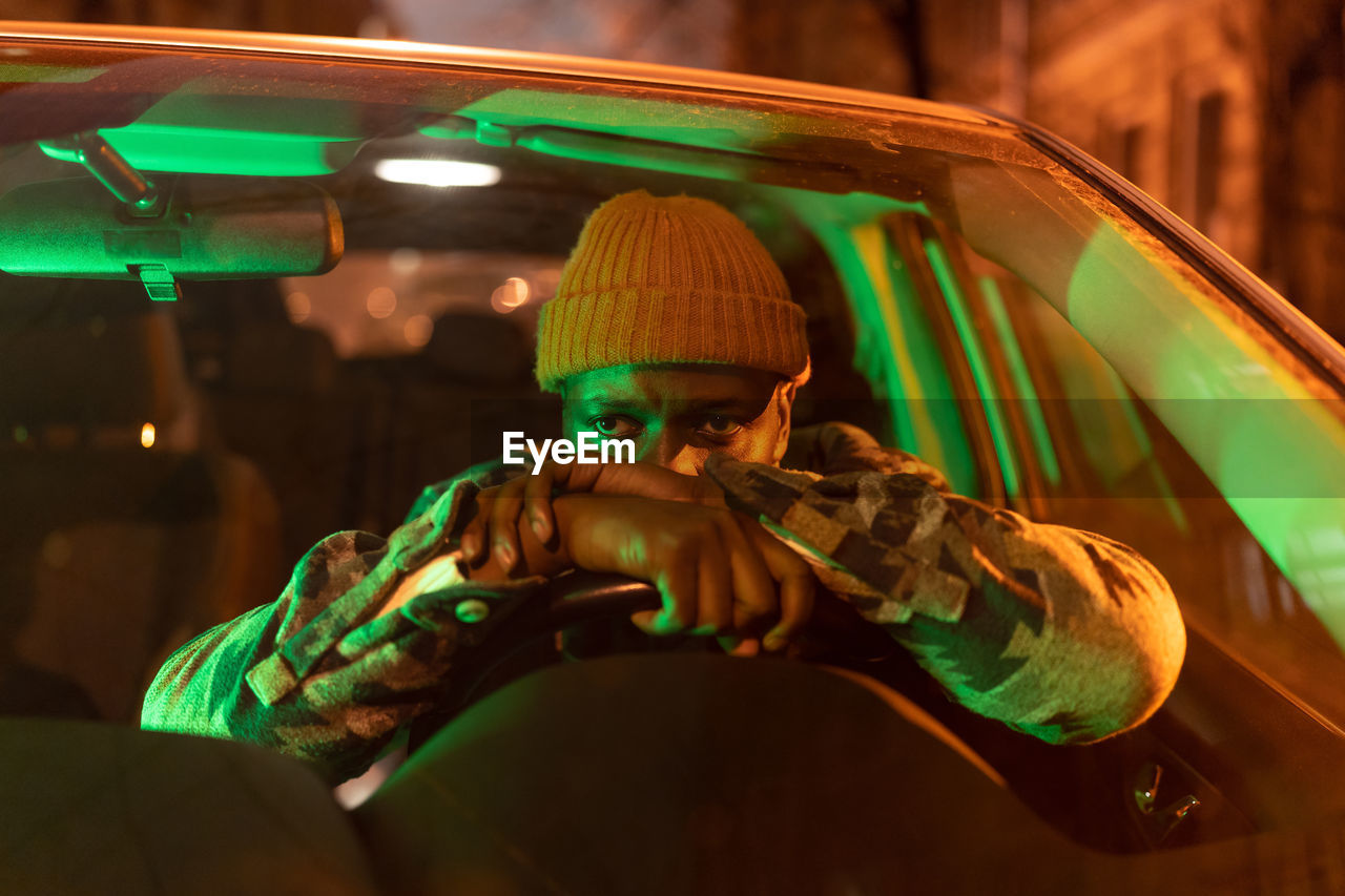 Worried african man in car at night, having life problems. depressed black guy behind steering wheel