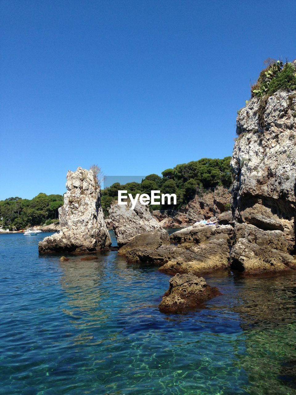 Rocks in sea against clear blue sky