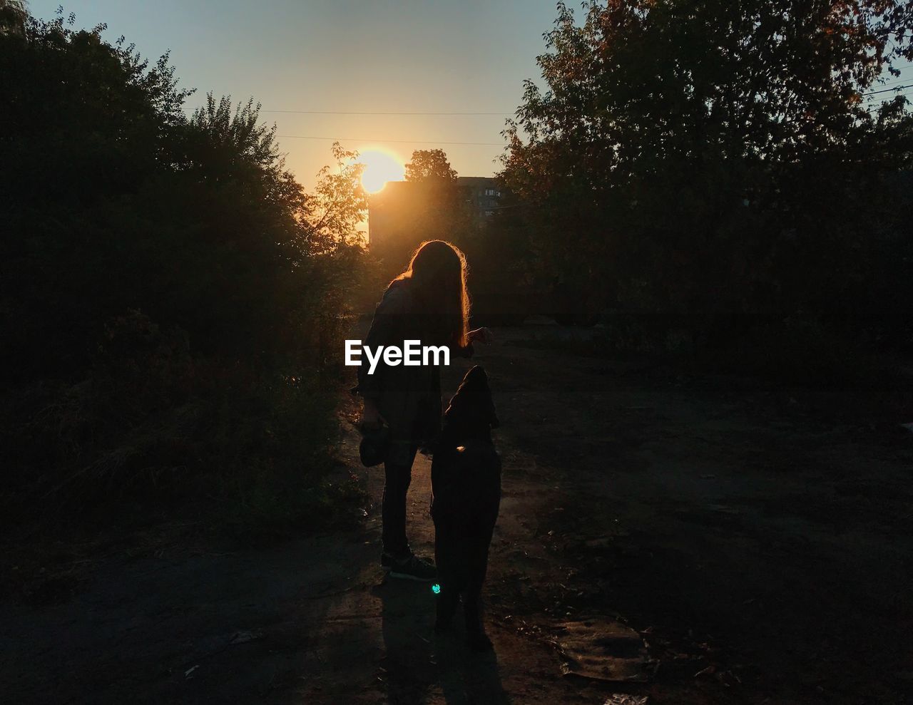 Silhouette of woman and child standing on footpath during sunset