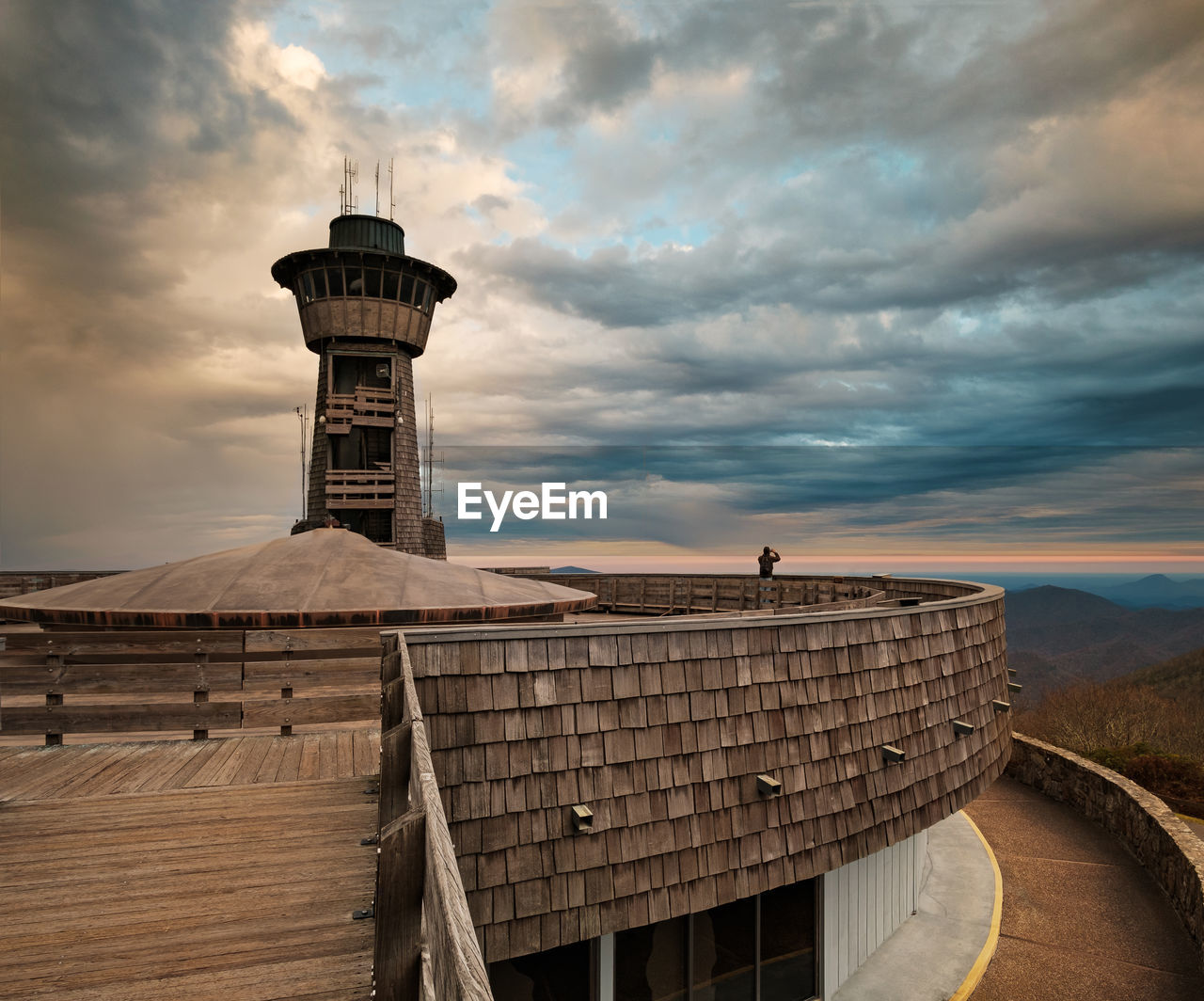 Lighthouse by building against sky during sunset