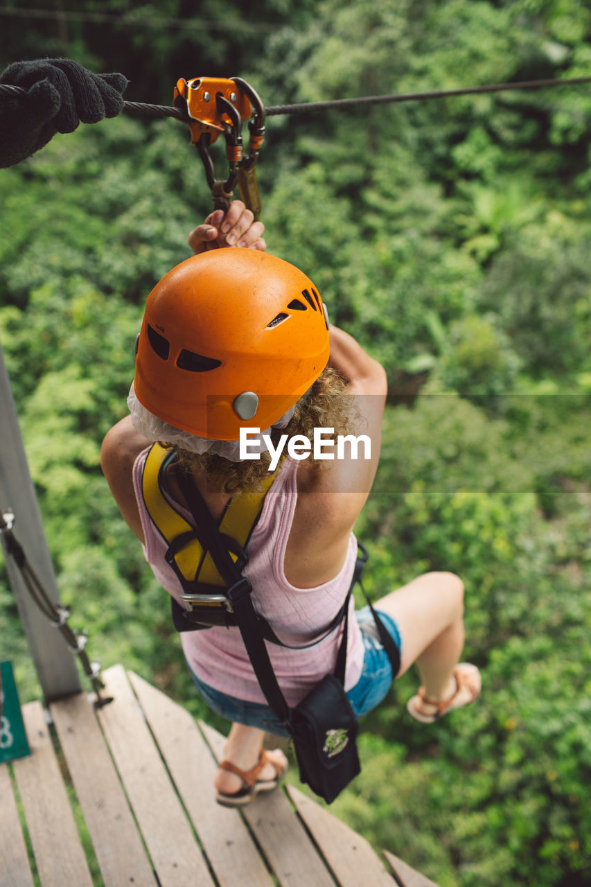 Full length of woman hanging on zip line over trees