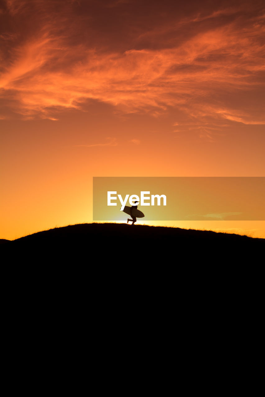 SILHOUETTE OF PERSON STANDING ON ORANGE SUNSET