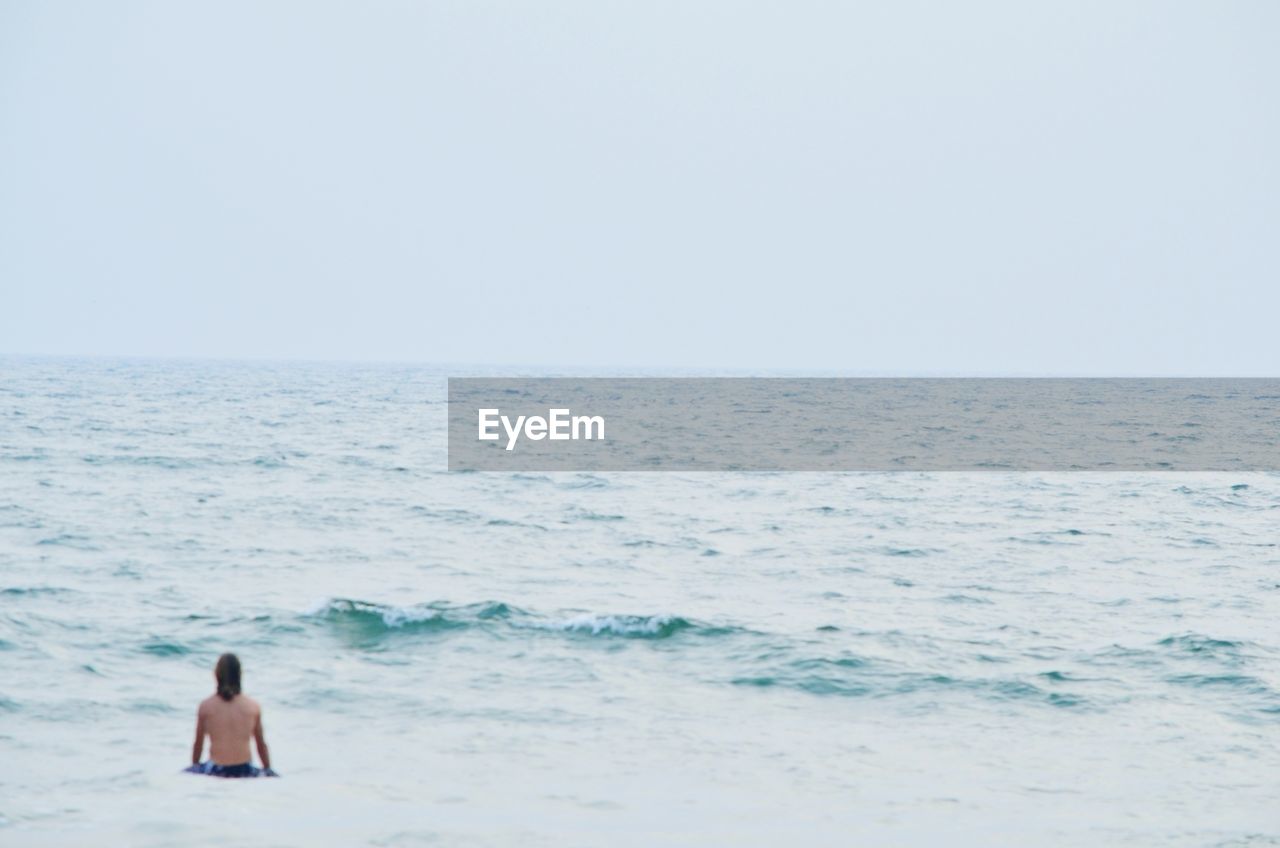 Rear view of woman standing on beach against clear sky