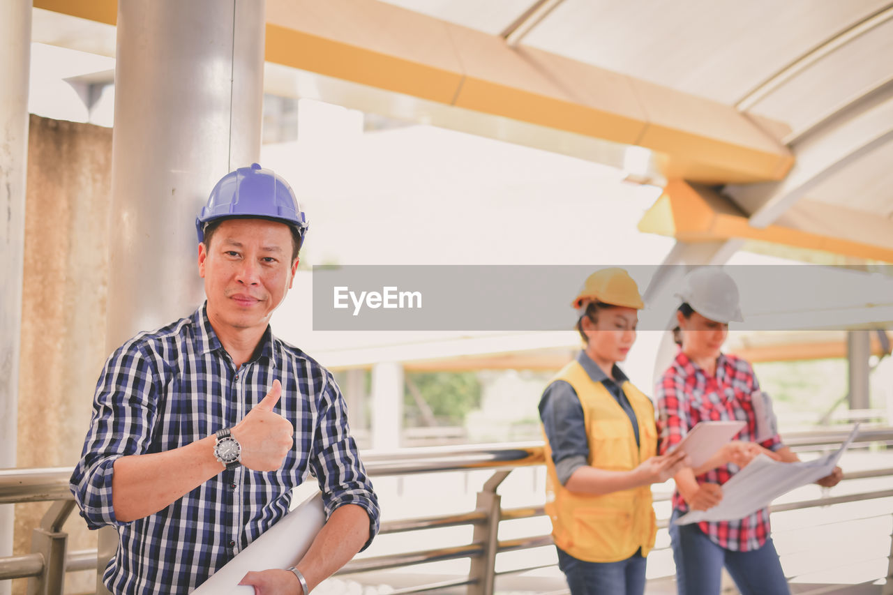 Portrait of male engineer showing thumbs up sign while standing by colleagues in bridge