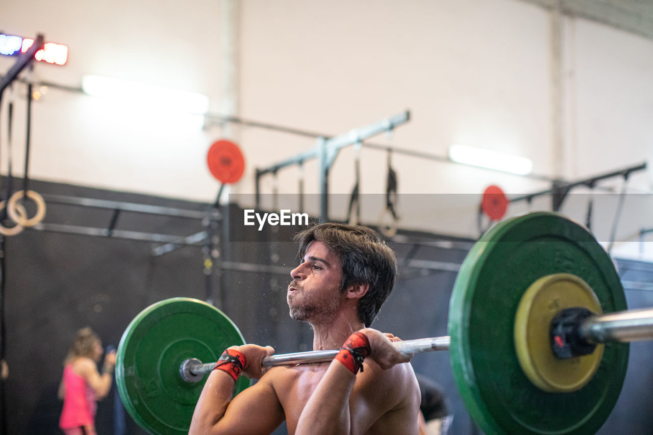 Muscular guy lifting barbell in modern gym