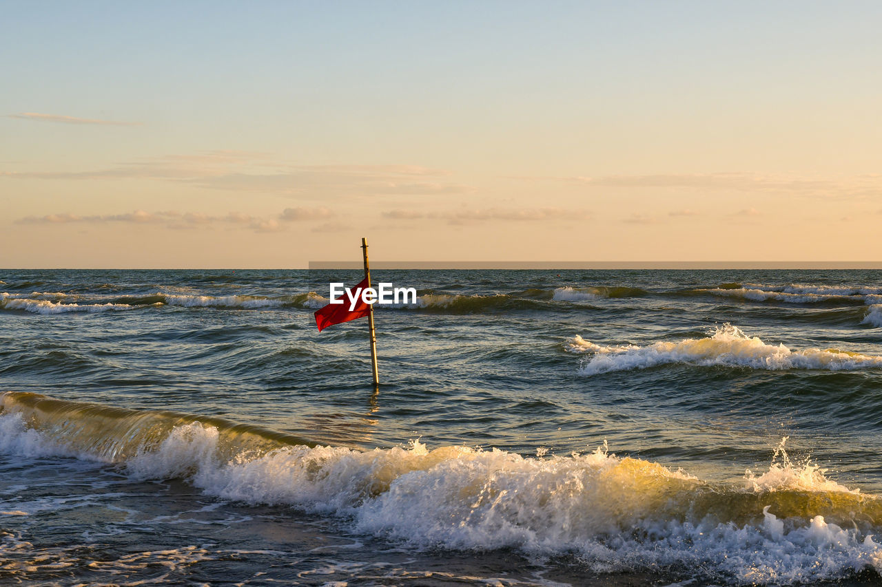 Scenic view of sea with a red flag against sky during sunset, tuscany, italy 