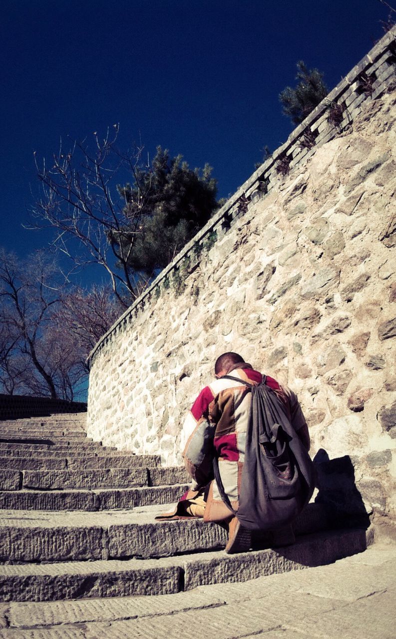 Rear view of man crouching on steps by stone wall