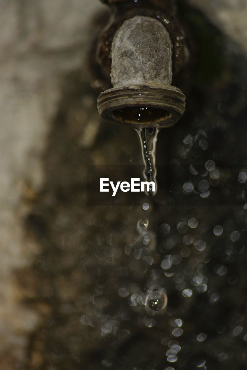 Close-up of water flowing from faucet against wall