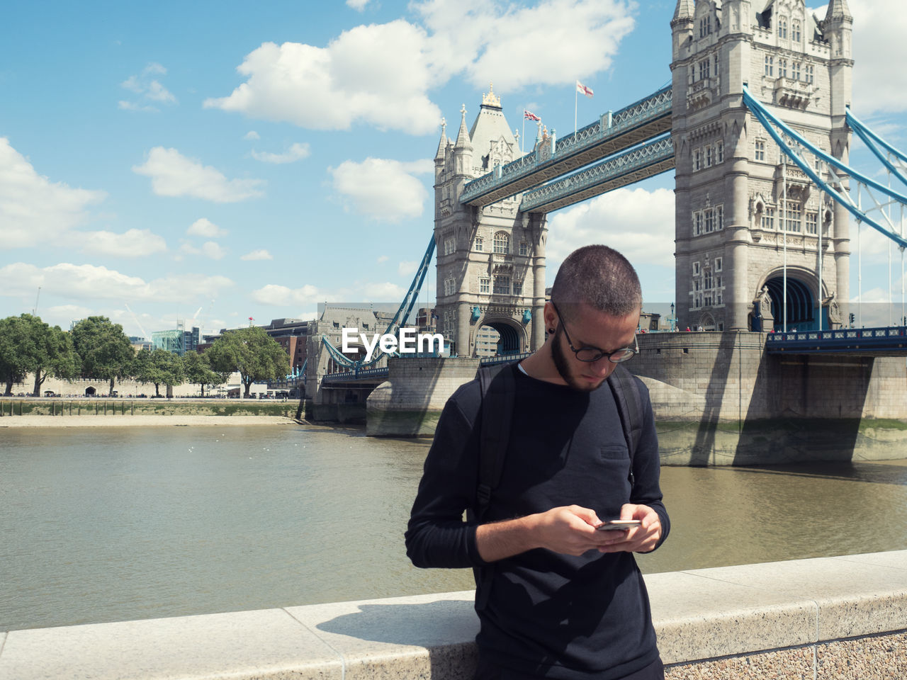 Man using mobile phone by tower bridge against sky