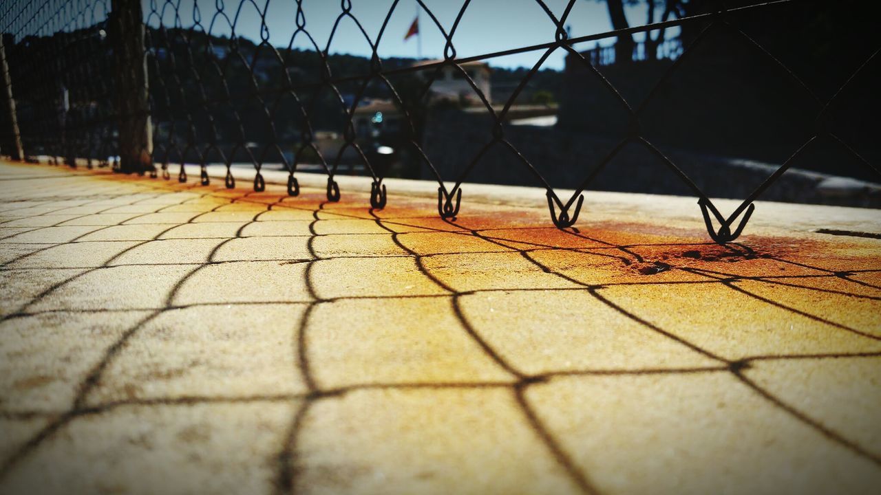 Shadow of chainlink fence on footpath