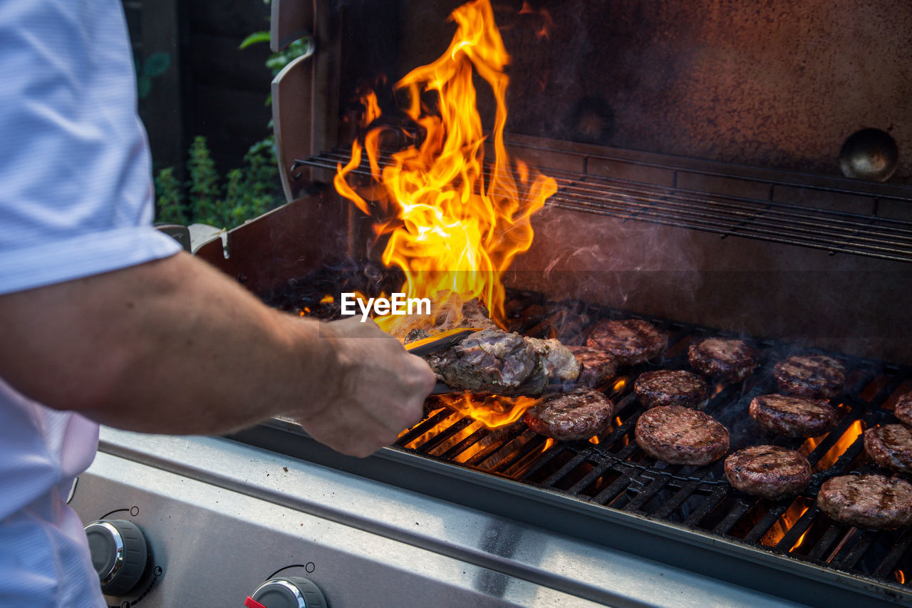 MIDSECTION OF MAN PREPARING FOOD ON BARBECUE