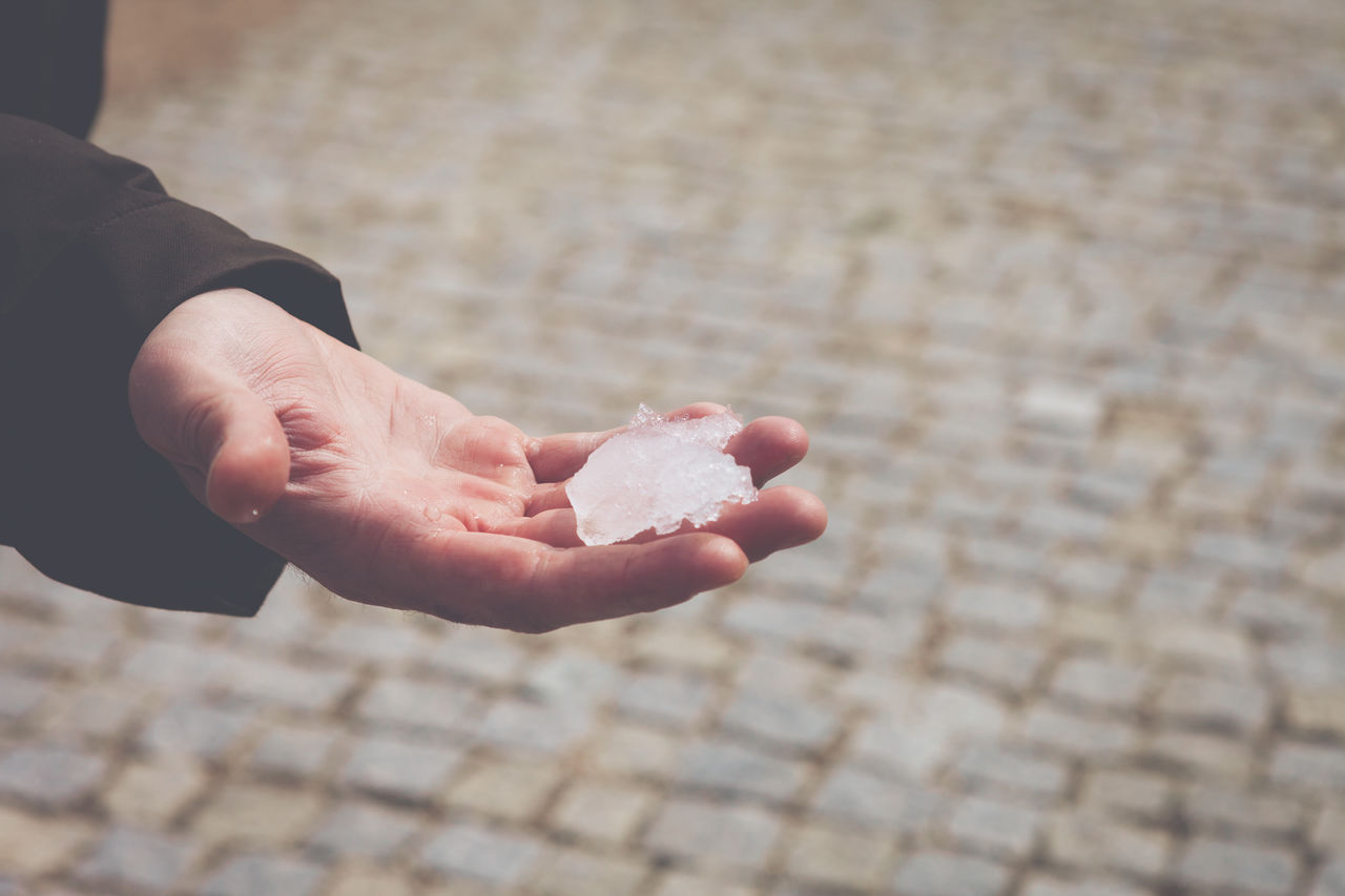 Cropped hand with snow over footpath