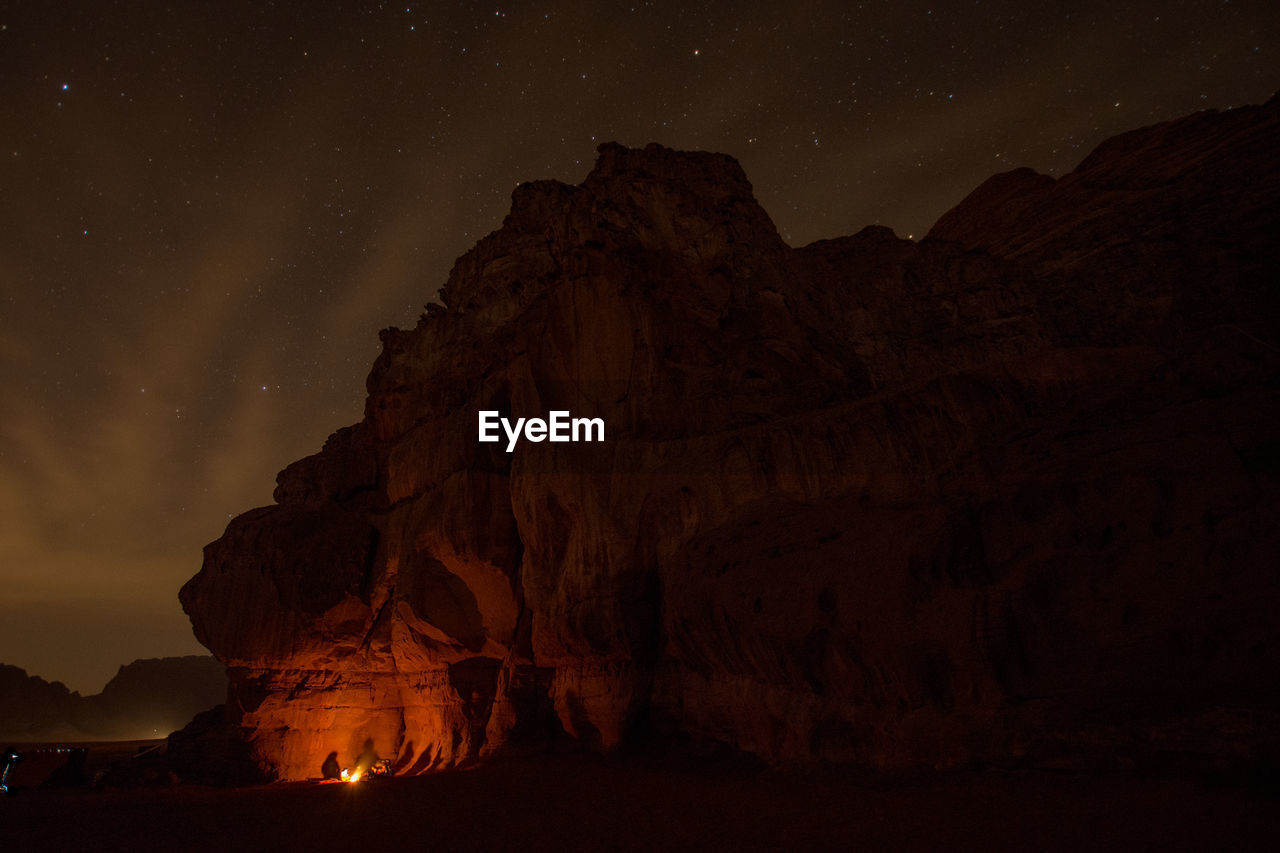 Fire by rock formations against sky at night