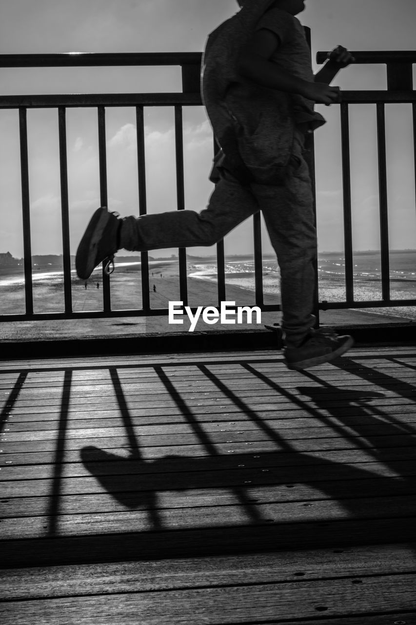 LOW SECTION OF MAN STANDING ON RAILING AGAINST SKY