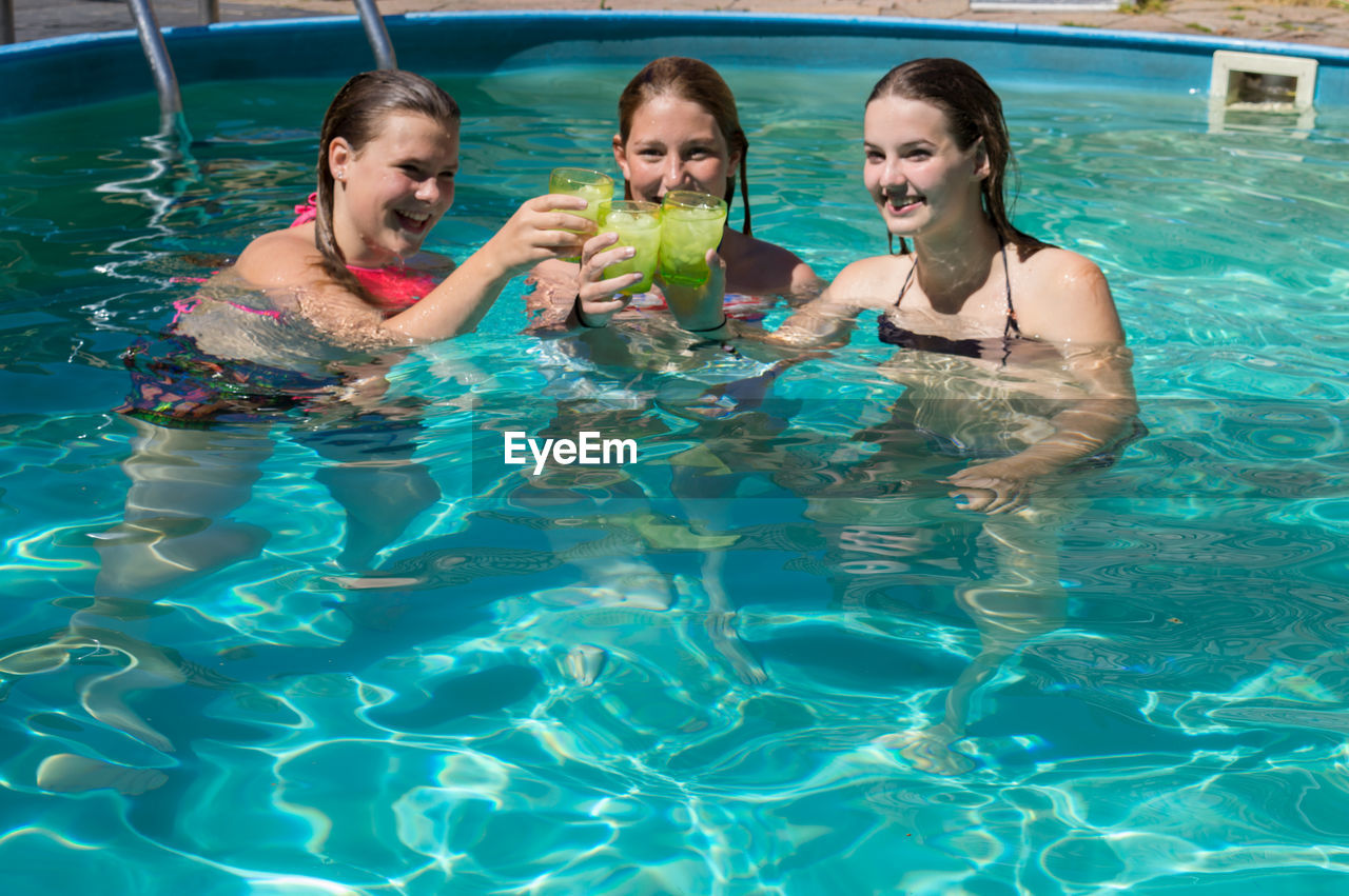 Happy female friends toasting drinks while enjoying in swimming pool