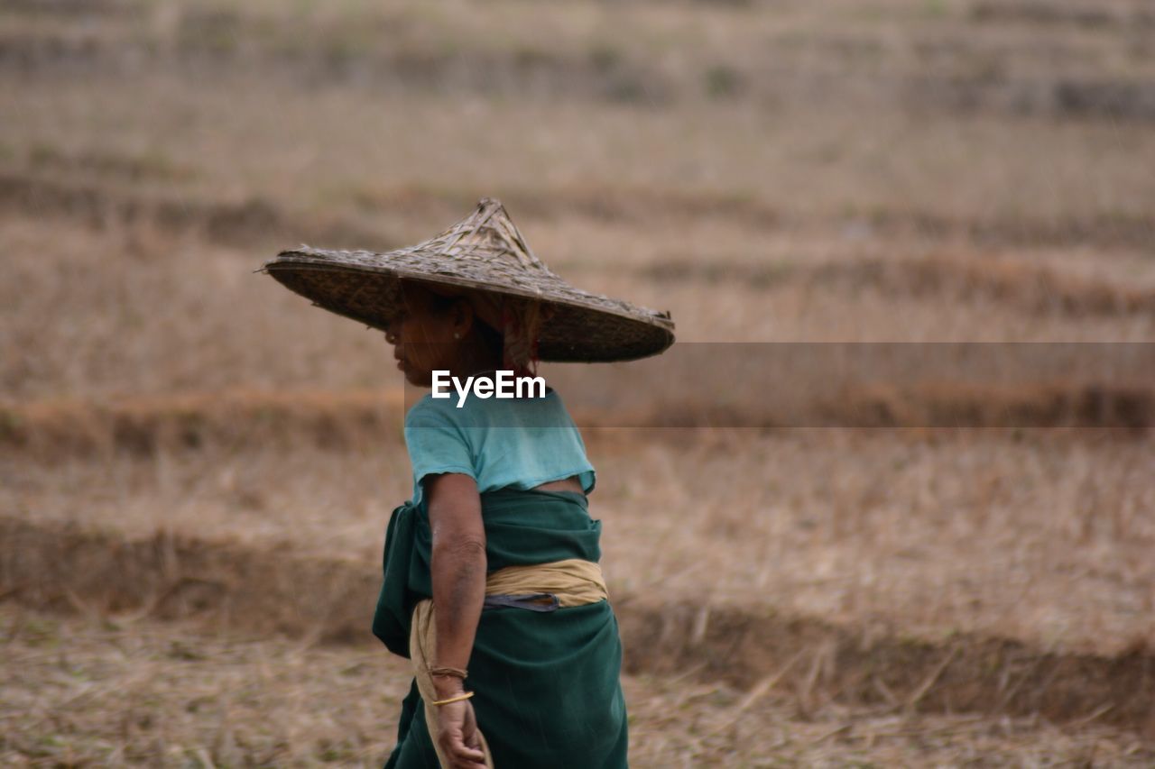 Rear view of woman wearing asian style conical hat on field