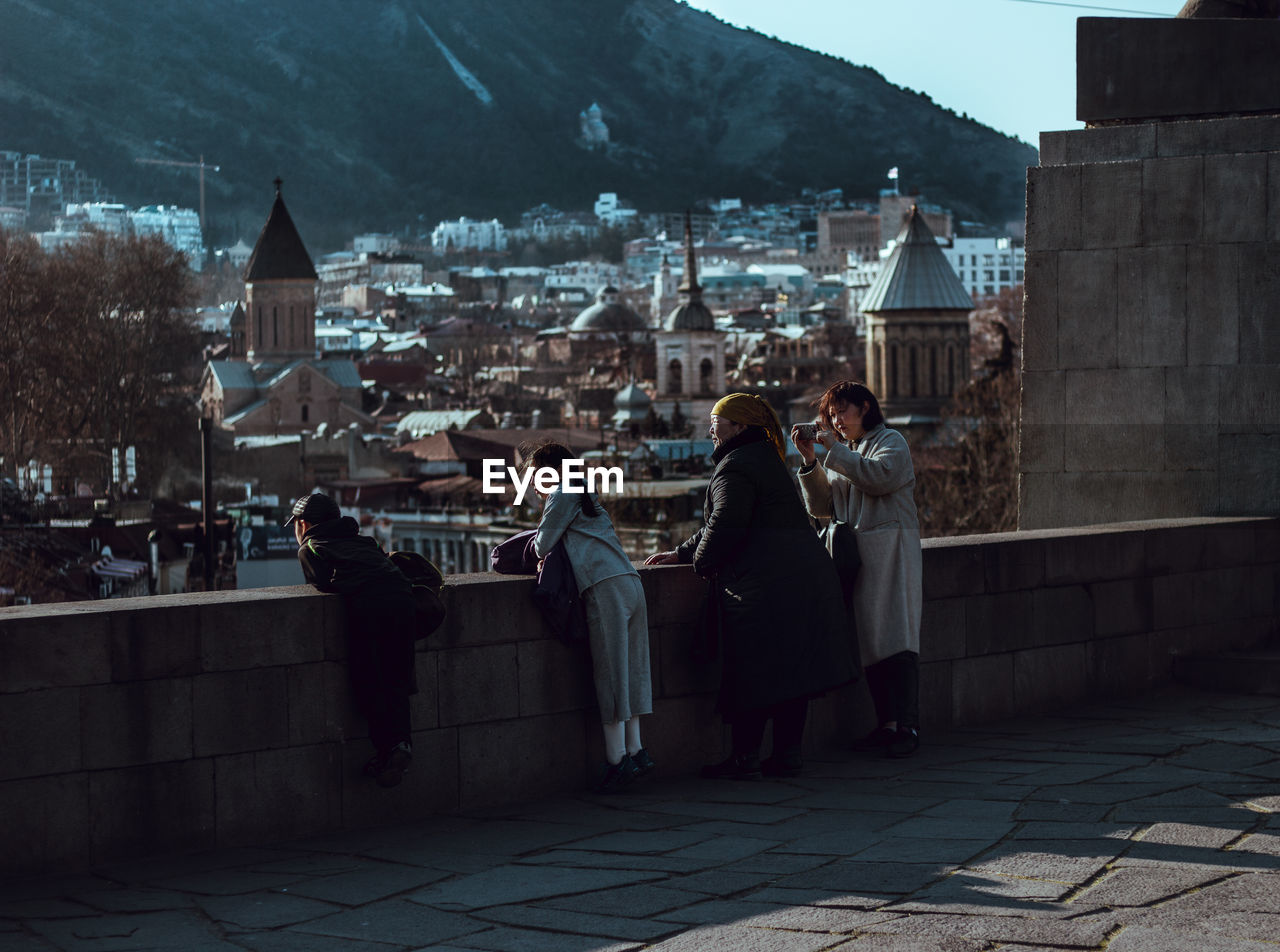 People looking at cityscape while standing by retaining wall