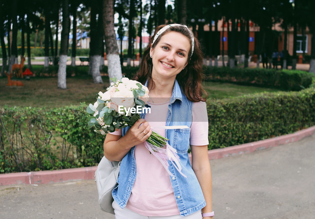 Portrait of smiling woman holding bouquet standing in park