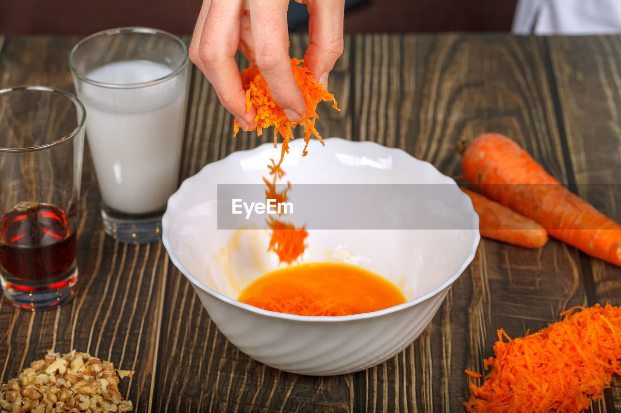 food and drink, food, hand, meal, one person, indoors, dish, carrot, healthy eating, bowl, freshness, wellbeing, household equipment, ingredient, adult, orange color, holding, pouring, produce, domestic room, lifestyles, vegetable, preparing food, table, kitchen utensil, spice, kitchen, close-up, breakfast