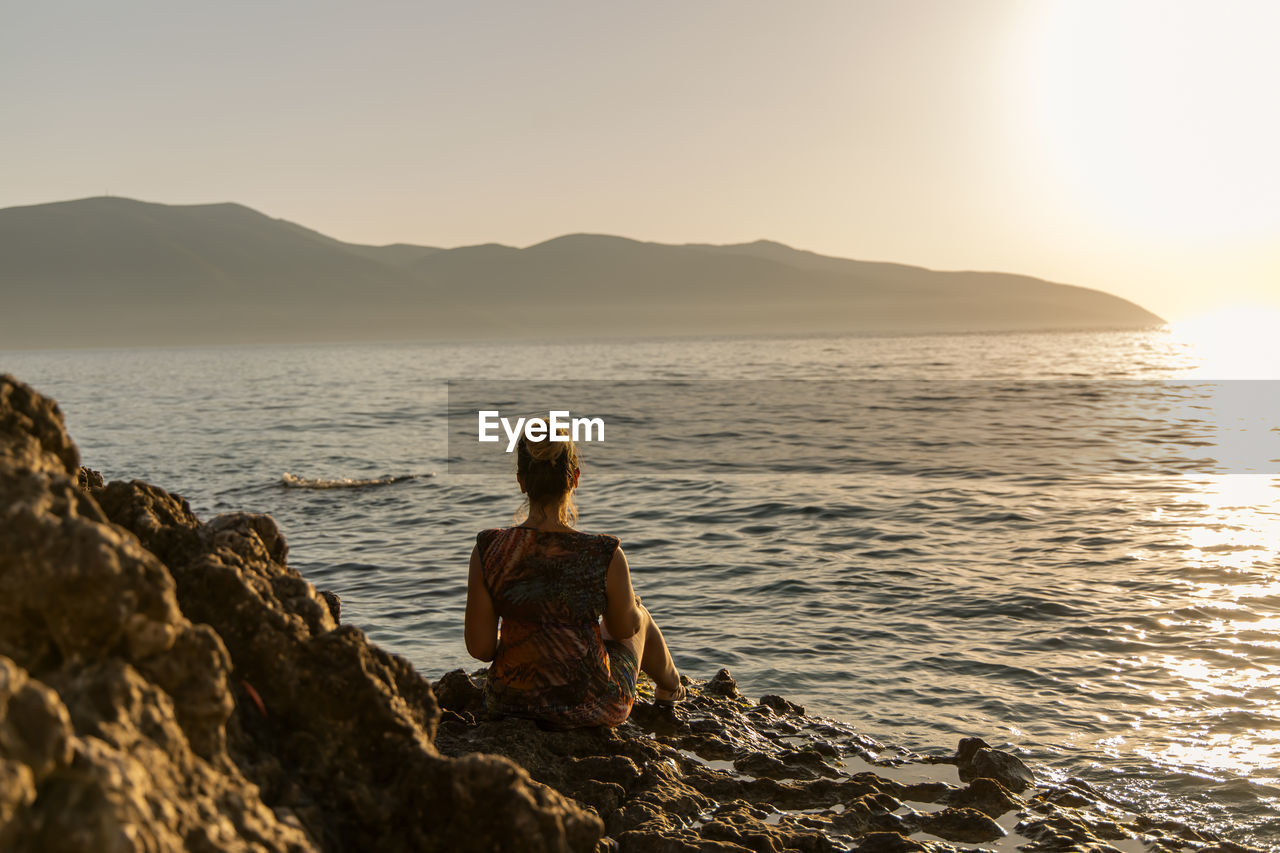 Rear view of woman standing at beach against clear sky