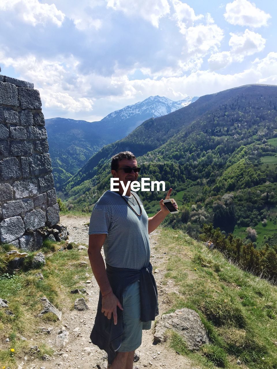 Portrait of smiling mature man with smart phone gesturing on mountain trail