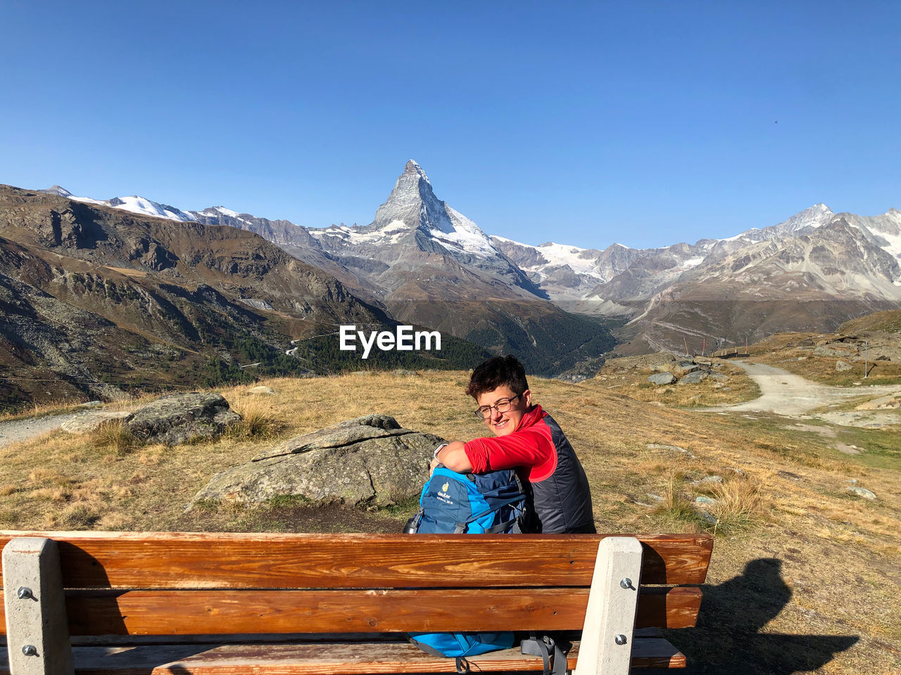 MAN SITTING ON WOOD AGAINST MOUNTAIN RANGE